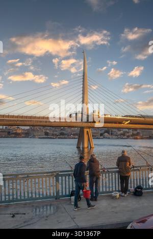Pescatori al tramonto di fronte al ponte della metropolitana Halic a Istanbul, Türkiye Foto Stock