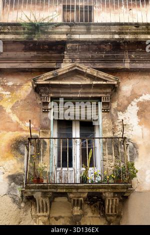 Ragusa, Sizilien - Italia - 04-03-2025: Balcone in pietra con ringhiere arrugginite, piante in vaso e facciata sbucciante su un vecchio edificio a Ragusa, Sici Foto Stock