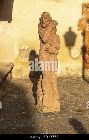Fordongianus - Sardinien - Italien - 03-04-2025: Una scultura astratta in pietra dalle forme umane sorge su un terreno acciottolato di fronte a Casa Aragonese, l Foto Stock