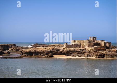 Rovine costiere di Essaouira, Marocco, con cieli limpidi e acque calme visibili a mezzogiorno Foto Stock