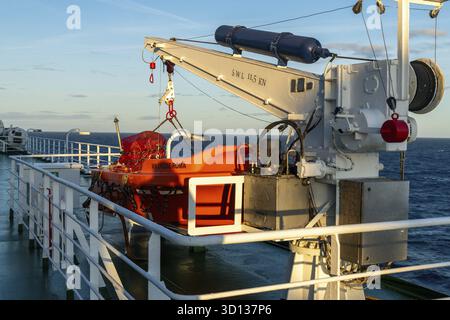 Barcellona, Catalogna - Spagna - 01-10-2025: Scialuppa di salvataggio arancione assicurata da una gru bianca sul ponte del traghetto in mare, contrassegnata con CROCIERA SUL molo DI ROMA in serata Foto Stock