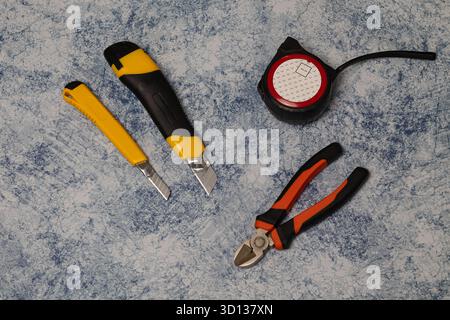 Sono disposti utensili manuali assortiti, tra cui coltelli, metro a nastro e pinze, mettendo in evidenza le apparecchiature essenziali per progetti fai da te Foto Stock