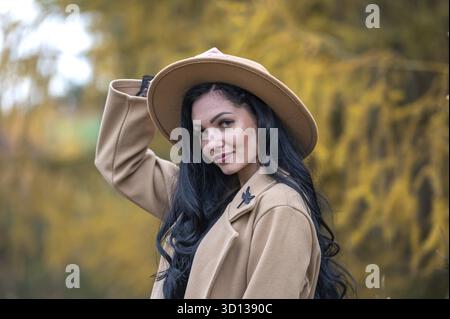 Ritratto all'aperto di una bella giovane donna bruna in un cappotto e un cappello beige Foto Stock