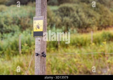 Cartello segnaletico recinzione elettrica con la mano e i fulmini su un palo di legno nel pascolo rurale. Concetto di pericolo e attenzione Foto Stock