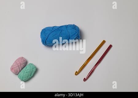 Palline colorate in filato rosa, verde e blu, con due ganci a uncinetto in oro e rosso, disposte su una superficie bianca pulita, perfette per la realizzazione di progetti Foto Stock