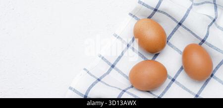 Uova di pollo su un asciugamano da cucina a quadri su un tavolo leggero. concetto di prodotti agricoli e alimenti naturali. Articoli e annunci su prodotti fatti in casa. Fresco Foto Stock