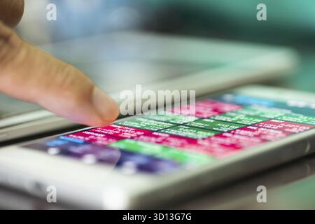 Vista macro dell'uomo che utilizza l'applicazione per il mercato azionario su uno smartphone touchscreen, profondità di messa a fuoco ridotta Foto Stock