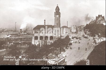 Una cartolina storica mostra il St. Pauli Landungsbrücken ad Amburgo. Le caratteristiche dominanti includono la torre dell'orologio e gli edifici terminali a cupola. A sinistra, le attività portuali e i battelli a vapore sono visibili dai moli. Il primo piano mostra una strada trafficata con tram, automobili e diversi pedoni. Da una cartolina originale. Pubblicato da C. Worzedialeck di Amburgo, anni 1920 Foto Stock
