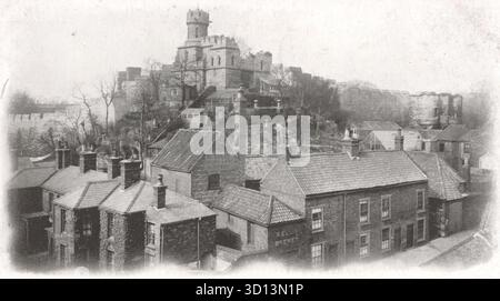 Una fotografia dai toni seppia cattura una vista alta delle mura medievali del Castello di Lincoln e della Torre di osservazione in cima a una ripida collina. Sotto le fortificazioni, un gruppo di tetti appartenenti a edifici della classe operaia o commerciali forma il primo piano. L'immagine sottolinea la drammatica altezza del castello e il contrasto urbano storico di Lincoln. Da una cartolina originale pubblicata da Boots come parte della loro Pelham Series, c1910. Foto Stock