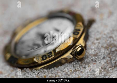 Un primo piano della corona di un vecchio orologio in ottone mezzo sepolto nella sabbia Foto Stock