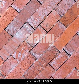 Vista ravvicinata di un motivo a spina di pesce fatto di mattoni rossi. I mattoni sono disposti in diagonale, mostrando la loro consistenza e le loro variazioni di colore Foto Stock
