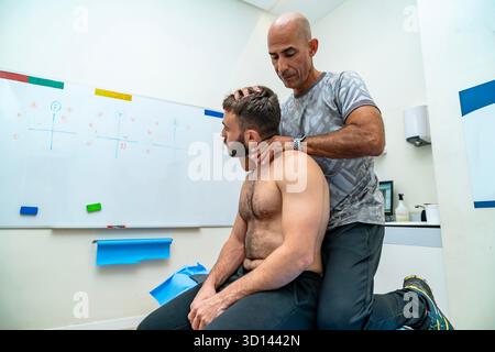 Fisioterapista che esegue la terapia manuale sul collo e sulle spalle di un uomo in una clinica Foto Stock