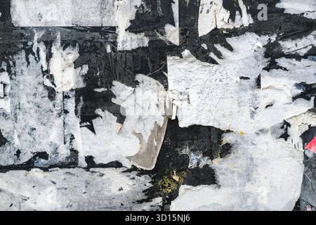 Grunge la consistenza di strati di carta strappati e poster usurati sulla vecchia parete con superficie ruvida. Sfondo astratto delle mura urbane intemprate, Foto Stock