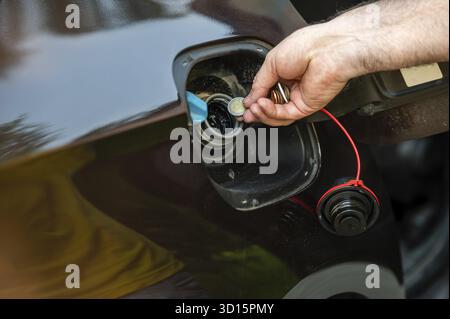 Mano d'uomo che mette le monete nel serbatoio dell'auto, primo piano, costoso concetto di carburante, crisi del carburante Foto Stock