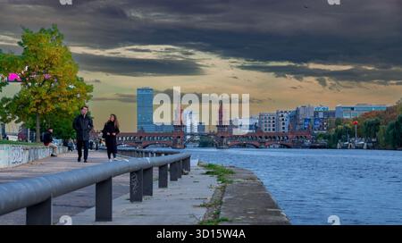Il ponte Oberbaum (Oberbaumbrücke) a Berlino, Germania, visto dal fiume lungo la Sprea. Due persone camminano lungo il fiume. Foto Stock