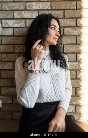 Donna alla moda che posa accanto a Un edificio in mattoni con luce soffusa, indossa Un comodo pullover e una gonna nera per catturare la moda autunnale minimalista. Foto Stock