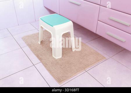 Sedia in plastica su moquette rettangolare beige in bagno. Poltroncina con piano verde per bambini. Armadio del bagno viola con cassetti. Stile minimalista Foto Stock