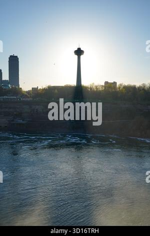 La Skylon Tower si erge sagomata contro il sole del tramonto mentre le luci fluiscono attraverso il fiume Niagara, catturate dal lato americano Foto Stock