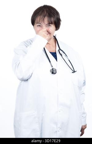 Medico in camice da laboratorio che pizzica il naso e fa un viso disgustato, reagendo a un forte odore sgradevole o cattivo odore in uno studio clinico Foto Stock