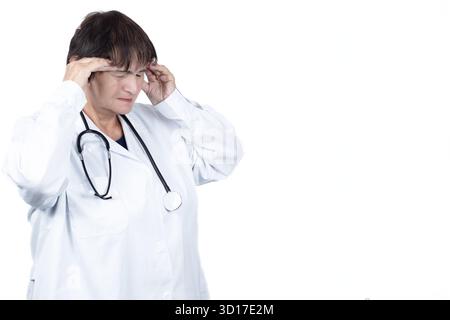 Medico donna in camice da laboratorio e stetoscopio che soffre di stress e mal di testa intensi, toccando le tempie con un'espressione dolorosa a causa delle lunghe ore Foto Stock