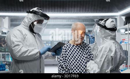 Esperto in una tuta protettiva studia la risposta immunitaria su pazienti infetti in quarantena, sperimentando nuovi vaccini e trattamenti antivirali per combattere il disastro globale e la crisi sanitaria. Telecamera B.. Foto Stock