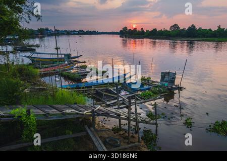 Le tradizionali barche da pesca in legno attraccate lungo una tranquilla riva del fiume durante l'alba, con riflessi sull'acqua e una tranquilla atmosfera rurale. Foto Stock