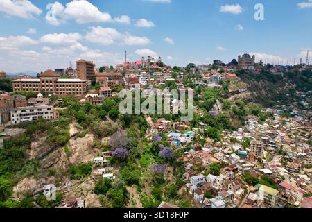 Antenna a metà pendenza della cresta di Analamanga che mostra il Palazzo di Andafiavaratra, il Palazzo della Regina (Rova), gli alberi di jacaranda e le storiche case collinari della città alta. Foto Stock