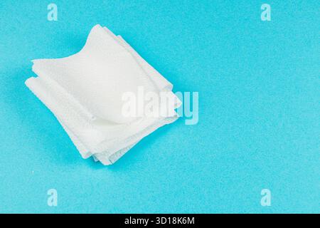 Le salviette bianche soffici sono impilate con cura su uno sfondo blu brillante, che ne mostra la disposizione e la consistenza. Ideale per varie attività di pulizia. Foto Stock