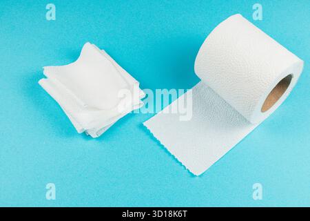 I morbidi asciugamani di carta bianca sono impilati in modo ordinato accanto a un rotolo srotolato su uno sfondo blu brillante, sottolineandone l'utilità per varie attività di pulizia Foto Stock