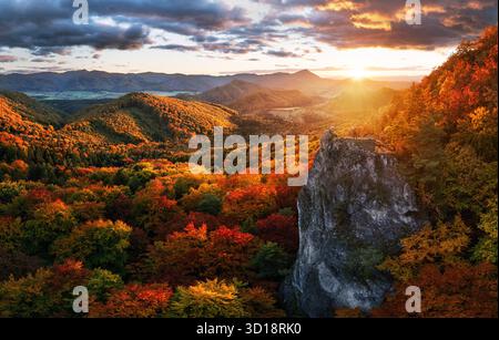 Uomo su pietra sulla collina e splendida valle di montagna nella foschia al tramonto colorato in autunno. Ragazzo, foresta rossa di montagna, cielo spettacolare con sole in autunno. Foto Stock
