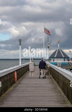 Coppie anziane o anziane che camminano insieme lungo lo storico molo in legno di Yarmouth, sulla costa dell'isola di wight, regno unito. Una coppia anziana sul molo. Foto Stock