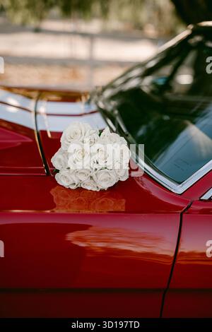 Boquet nuziale con rose bianche sopra un'auto d'epoca rossa Foto Stock
