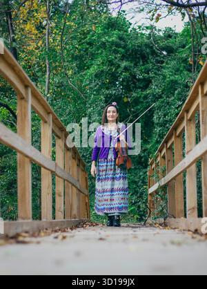 Una donna sta su un ponte di legno che regge un violino Foto Stock