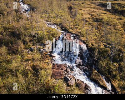 Vista aerea di una splendida cascata di montagna che si tuffa attraverso una vivace foresta di betulle verde in Norvegia. Foto Stock