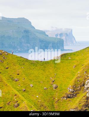 Vista delle vivaci colline verdi che si snodano verso il mare, con lontane scogliere avvolte dalla nebbia, che creano un paesaggio sereno ma selvaggio, il faro di Kallur, Norðoya, le Isole Faroe. Foto Stock