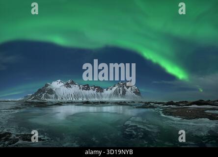 Vista delle danze dell'aurora boreale sopra le montagne innevate e la costa ghiacciata nell'abbraccio invernale dell'Islanda, Höfn, Islanda. Foto Stock
