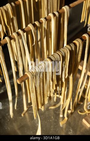 Pasta di Linguine fresca fatta in casa che si asciuga, su una cornice di legno, in primo piano. Cucina casalinga tradizionale e concetto di alimentazione sana. Foto Stock