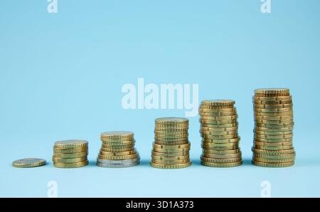 Pile di monete di dimensioni crescenti su sfondo studio di colore blu. Foto Stock