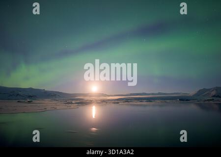 La vista dell'eterea aurora boreale danzerà sopra la laguna ghiacciata, con i suoi tendini verdi che rispecchiano il chiaro di luna sull'acqua ferma, Jokulsarlon, Sveitarfélagið Hornafjörður, Islanda. Foto Stock
