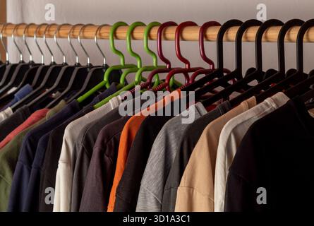 Magliette colorate allineate fianco a fianco su grucce. Appendiabiti su appendiabiti in legno. Foto Stock