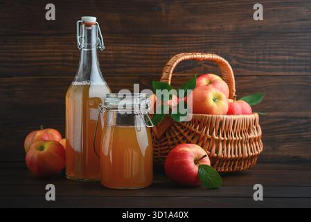 Sidro di mele in bottiglie di vetro e mele rosse nel cestello su sfondo di legno Foto Stock