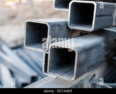 I profili in acciaio si sovrappongono l'uno sull'altro nel cantiere. Messa a fuoco selettiva su pila di profili in acciaio quadrati. Foto Stock