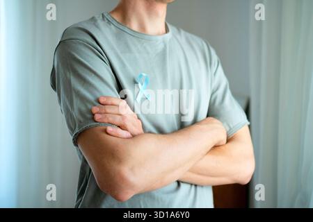 Uomo in piedi con le braccia incrociate che indossa un nastro di raso blu sulla camicia. Concetto di consapevolezza del cancro alla prostata a novembre, prevenzione, diagnosi precoce e assistenza medica per la salute maschile. Foto Stock