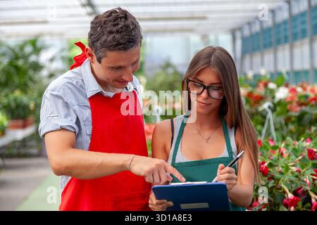 Due fioristi che lavorano insieme, rivedono gli appunti in una serra Foto Stock