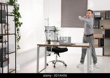 Giovane uomo d'affari che fa esercizio di stretching in ufficio Foto Stock