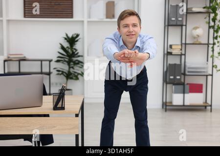 Giovane uomo d'affari che fa esercizio di stretching in ufficio Foto Stock