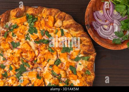 Pizza audace condita con pezzi speziati di pollo di bufala, fette di cipolla rossa e coriandolo fresco su una crosta dorata. Foto Stock