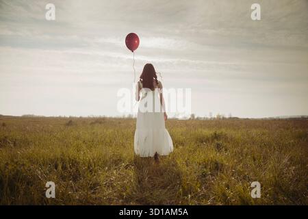 Donna con palloncino rosso nel silenzio del campo, sogno di libertà Foto Stock