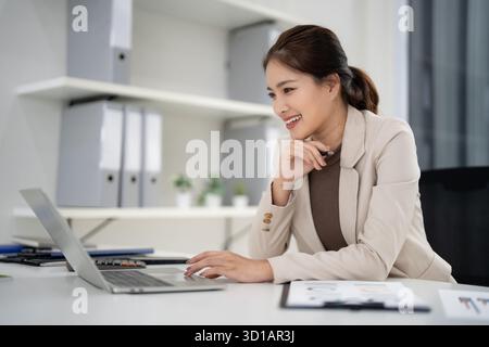 Donna asiatica professionista immobiliare si impegna con i clienti su un laptop in un ambiente ufficio luminoso agente di vendita di successo che lavora diligentemente Foto Stock