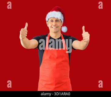 Uomo che indossa il grembiule rosso di un dipendente che fa un gesto positivo con la mano, con i pollici in alto sorridente e felice. Espressione allegra e vincitrice durante il wearin Foto Stock